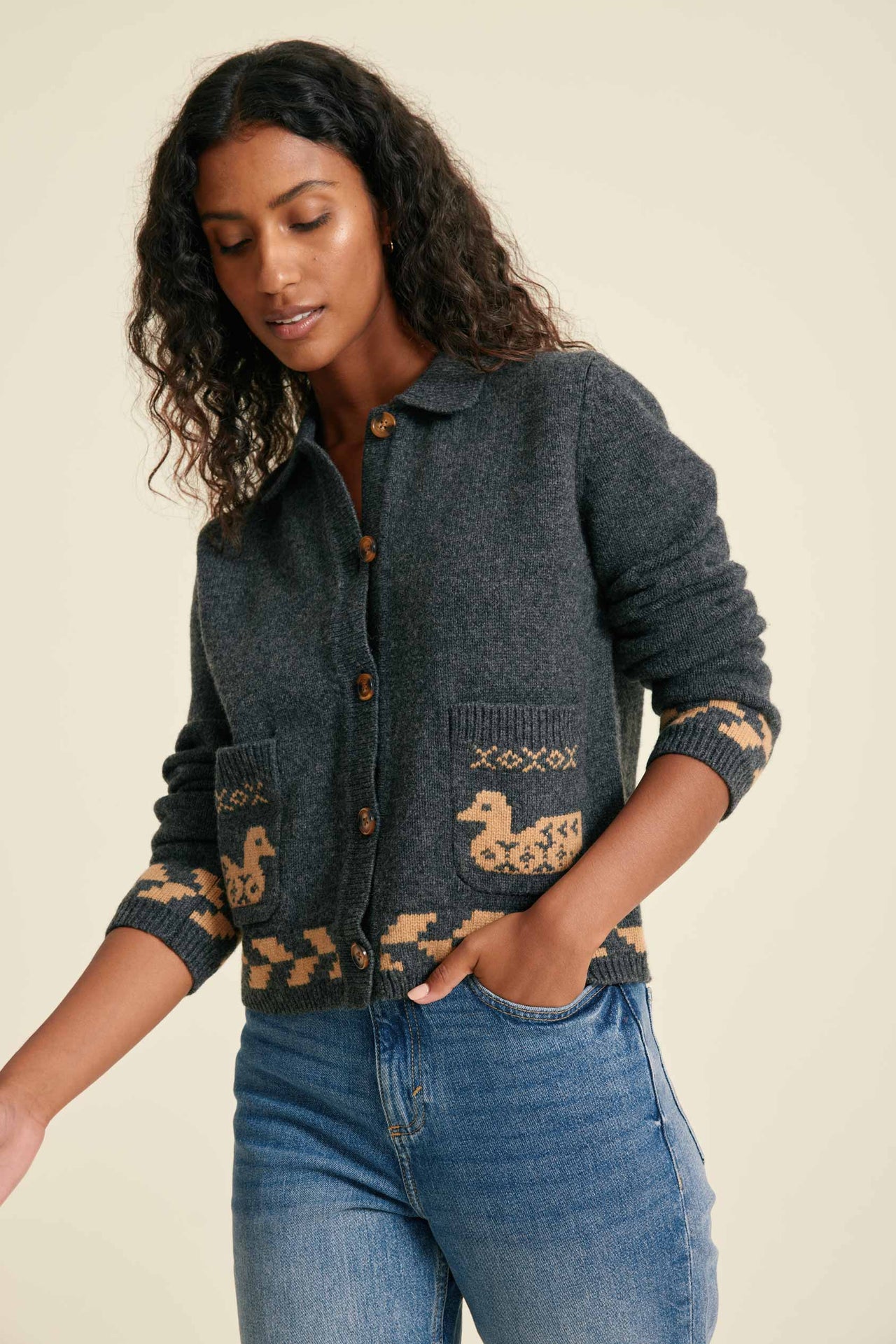 Woman wearing a dark gray knitted cardigan with duck pattern on a beige background