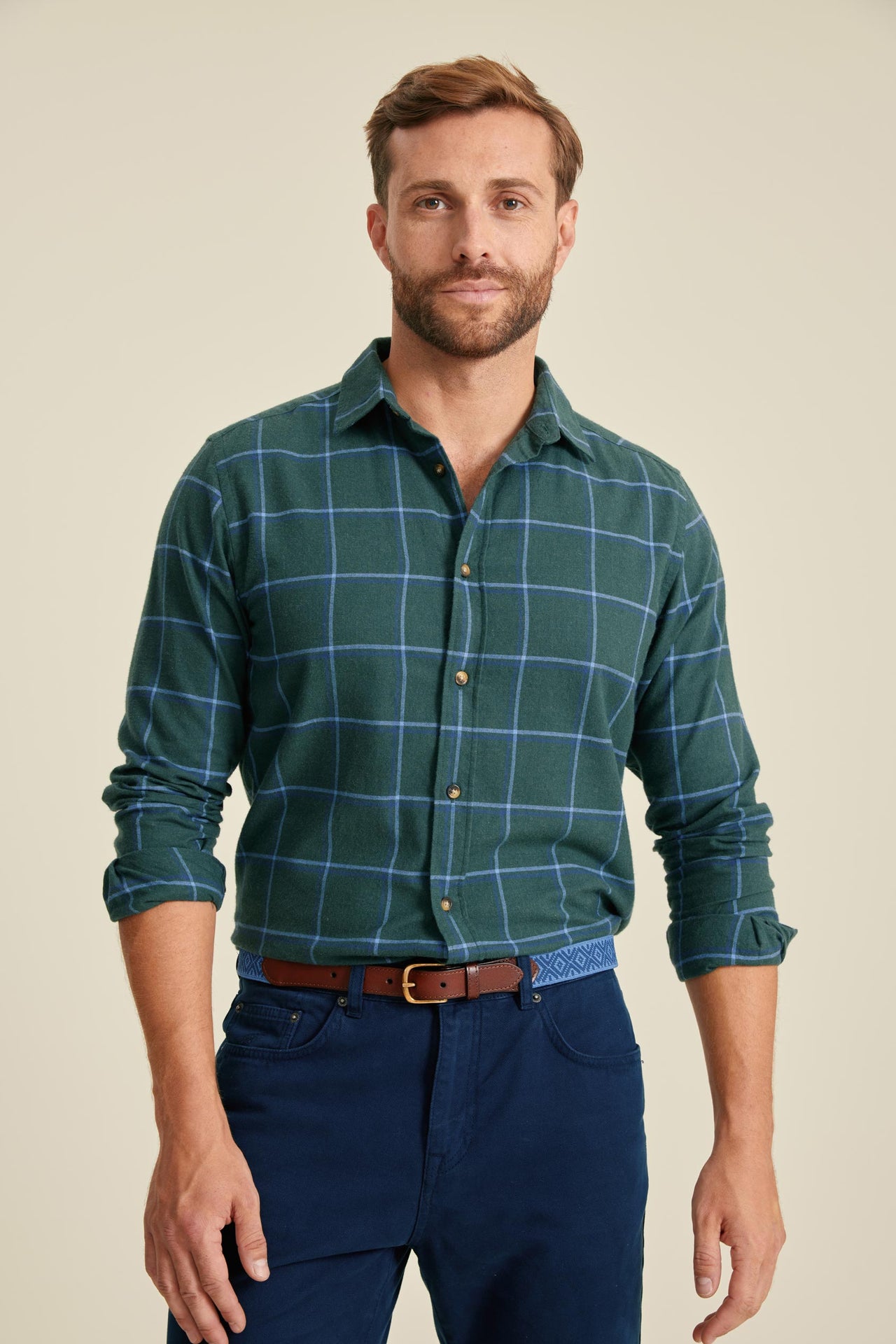 Man wearing a green plaid shirt and blue pants on a beige background