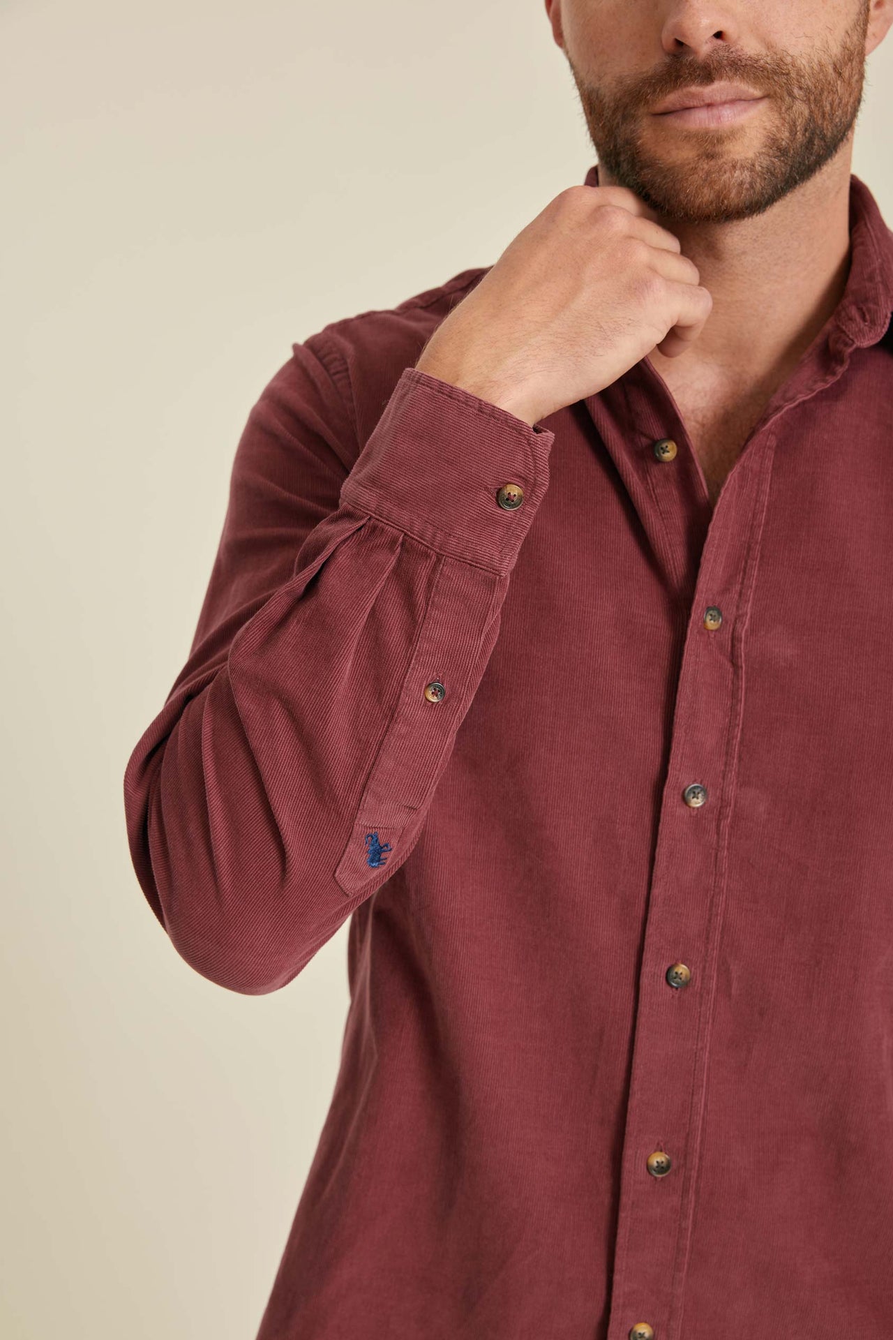Man wearing a burgundy shirt with rolled-up sleeves against a beige background