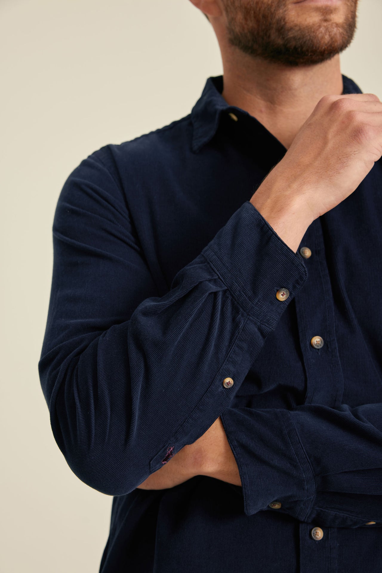 Navy blue shirt with gold buttons worn by a person on a beige background