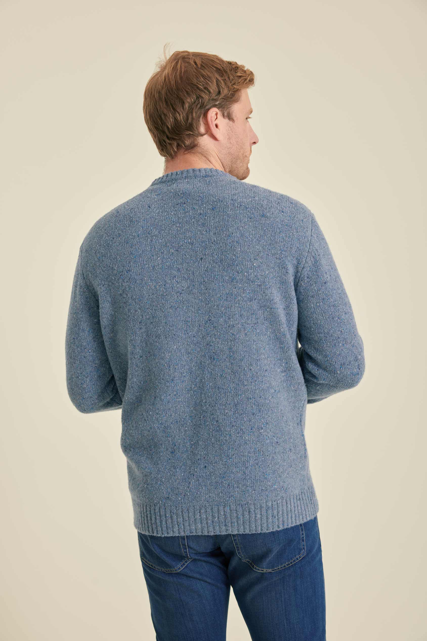 Man wearing a blue sweater and jeans on a beige background