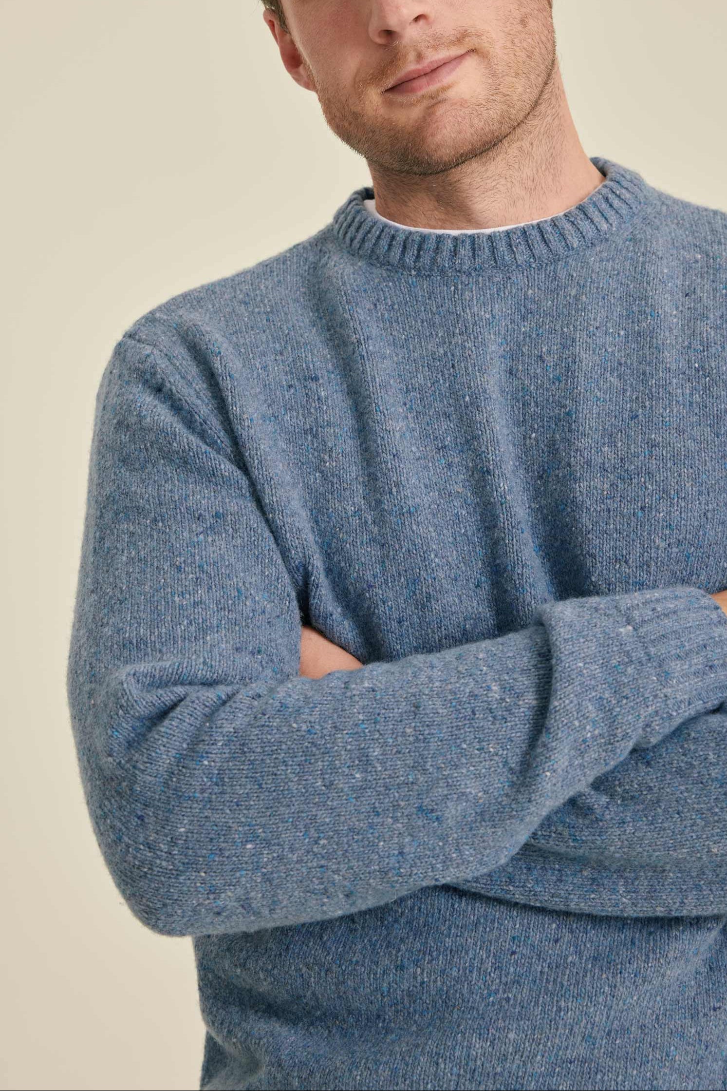 Man wearing a blue sweater with arms crossed against a beige background