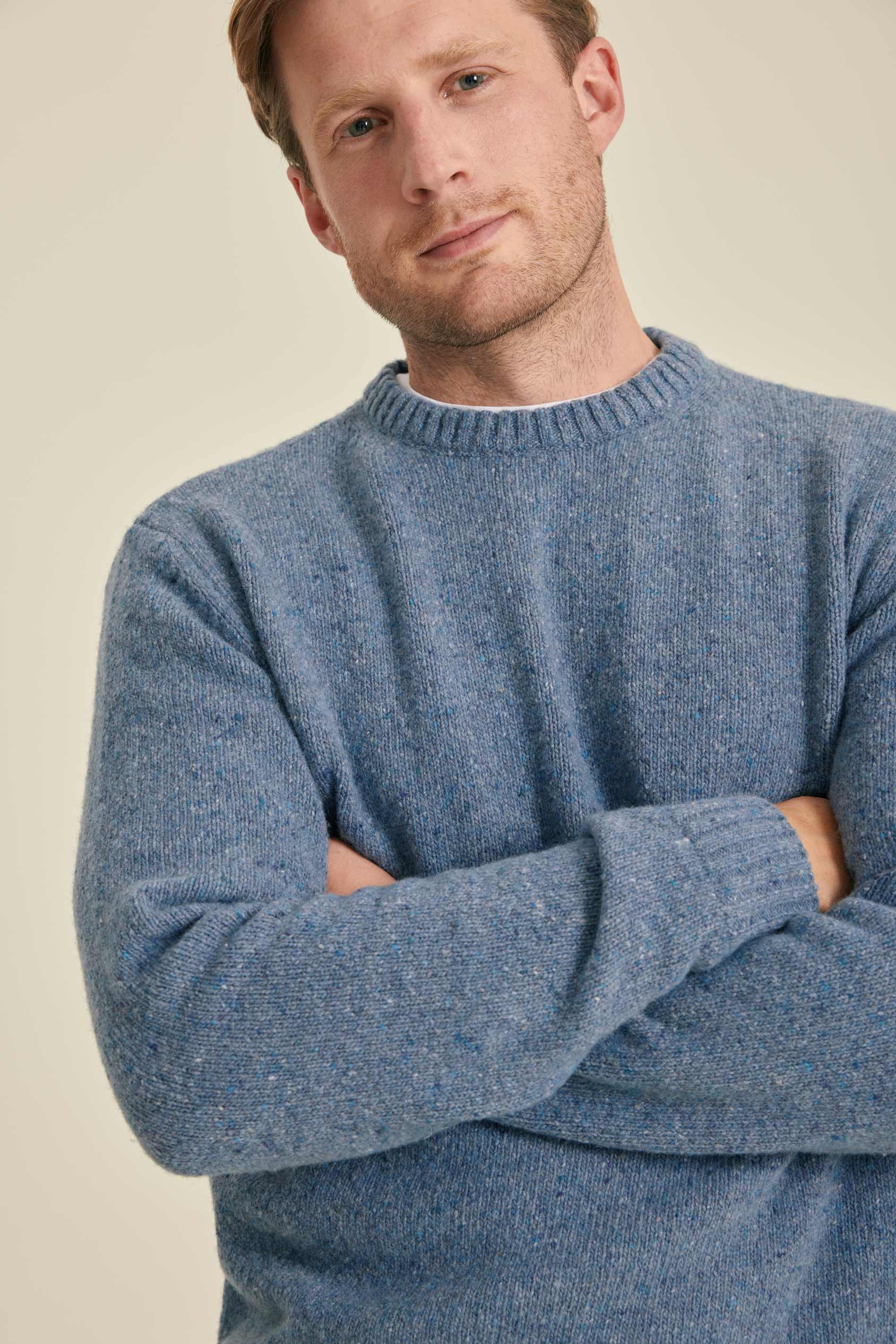 Man wearing a blue sweater with arms crossed against a beige background