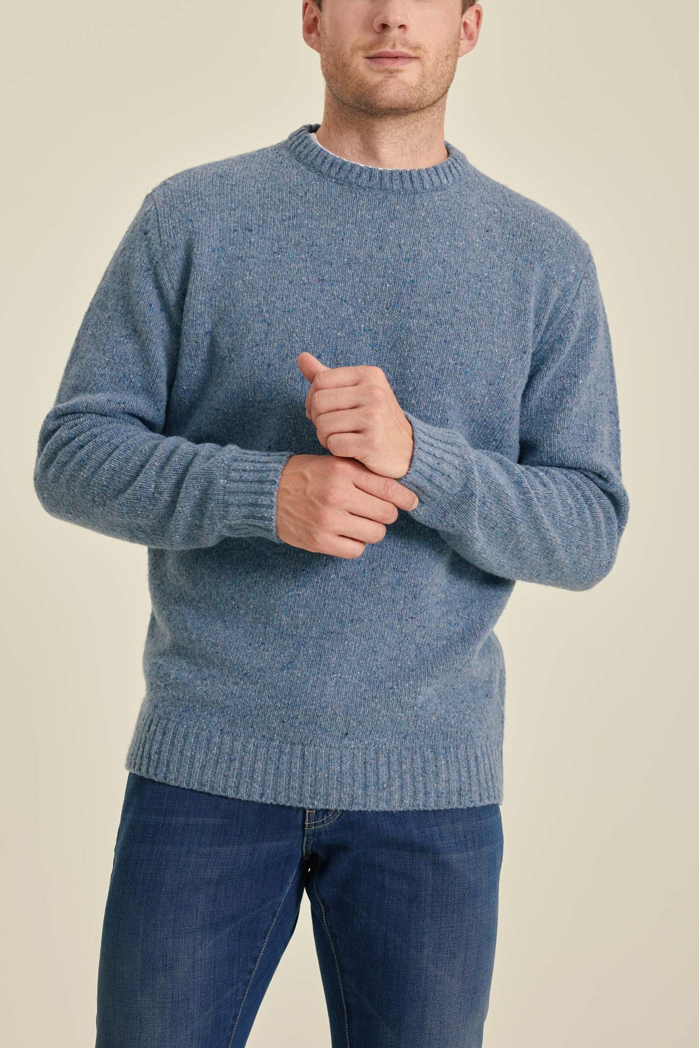 Man wearing a blue sweater and jeans against a beige background