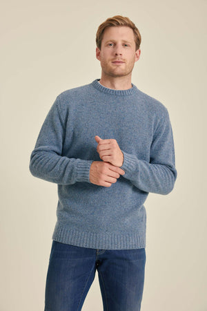 Man wearing a blue sweater and jeans against a beige background