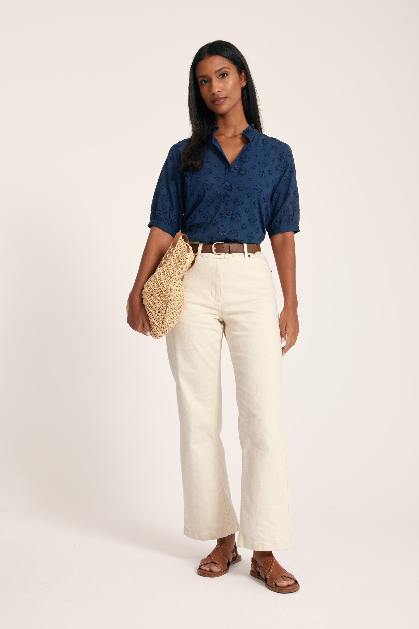 Woman wearing a blue shirt, white pants, and brown sandals on a white background
