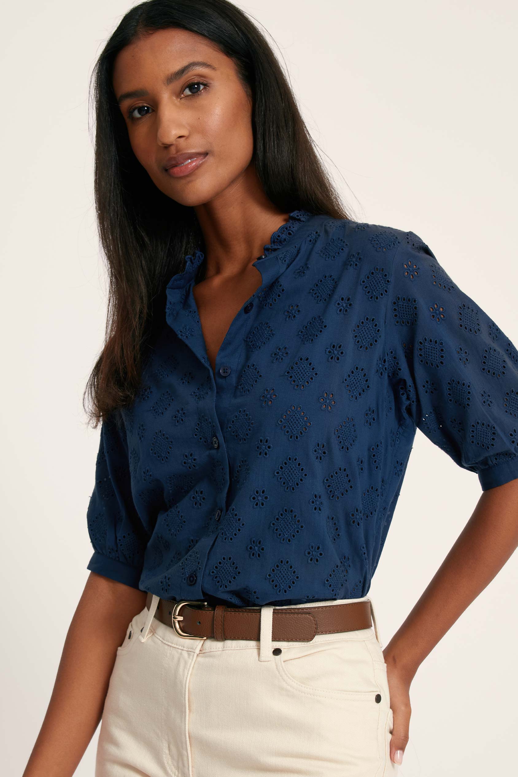 Woman wearing a blue patterned blouse and white pants on a plain background