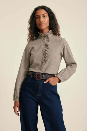 Woman wearing a patterned blouse and blue jeans against a beige background
