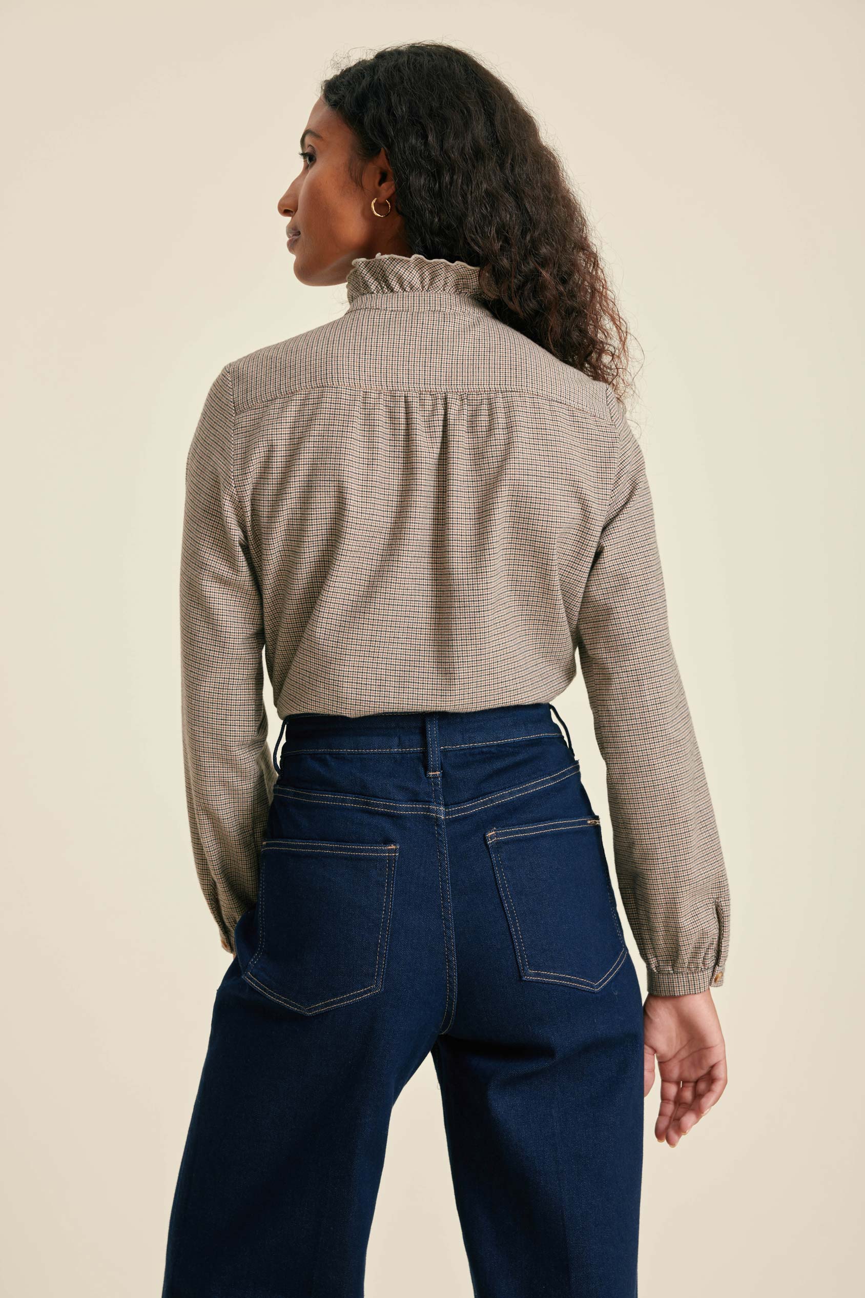 Woman wearing a checkered shirt and blue jeans against a beige background