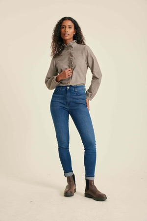 Woman wearing a beige shirt, blue jeans, and brown boots on a beige background