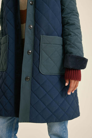 Person wearing a blue quilted coat with a neutral background