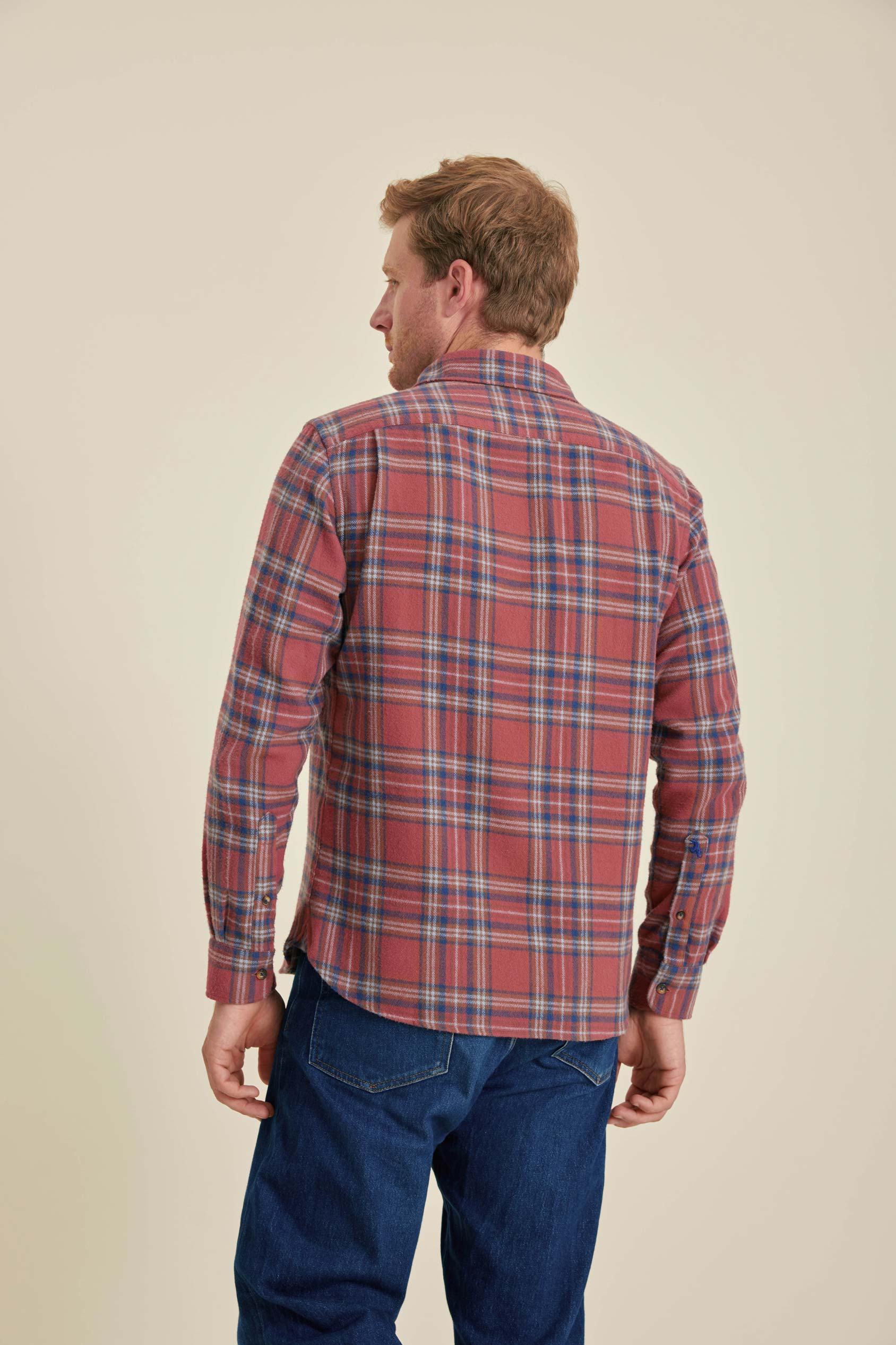 Man wearing a red plaid shirt and blue jeans on a beige background