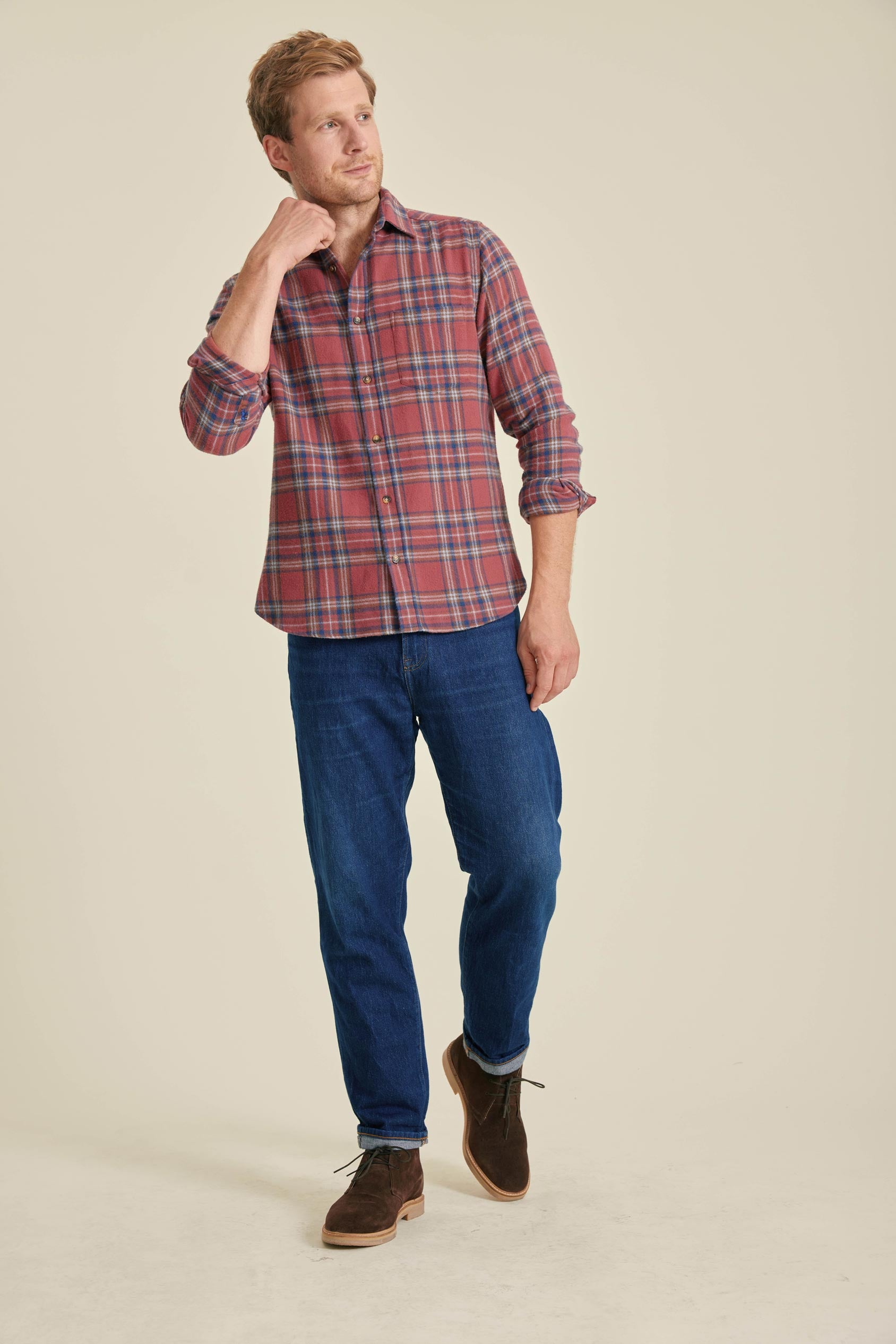 Man wearing a red plaid shirt, blue jeans, and brown shoes on a beige background