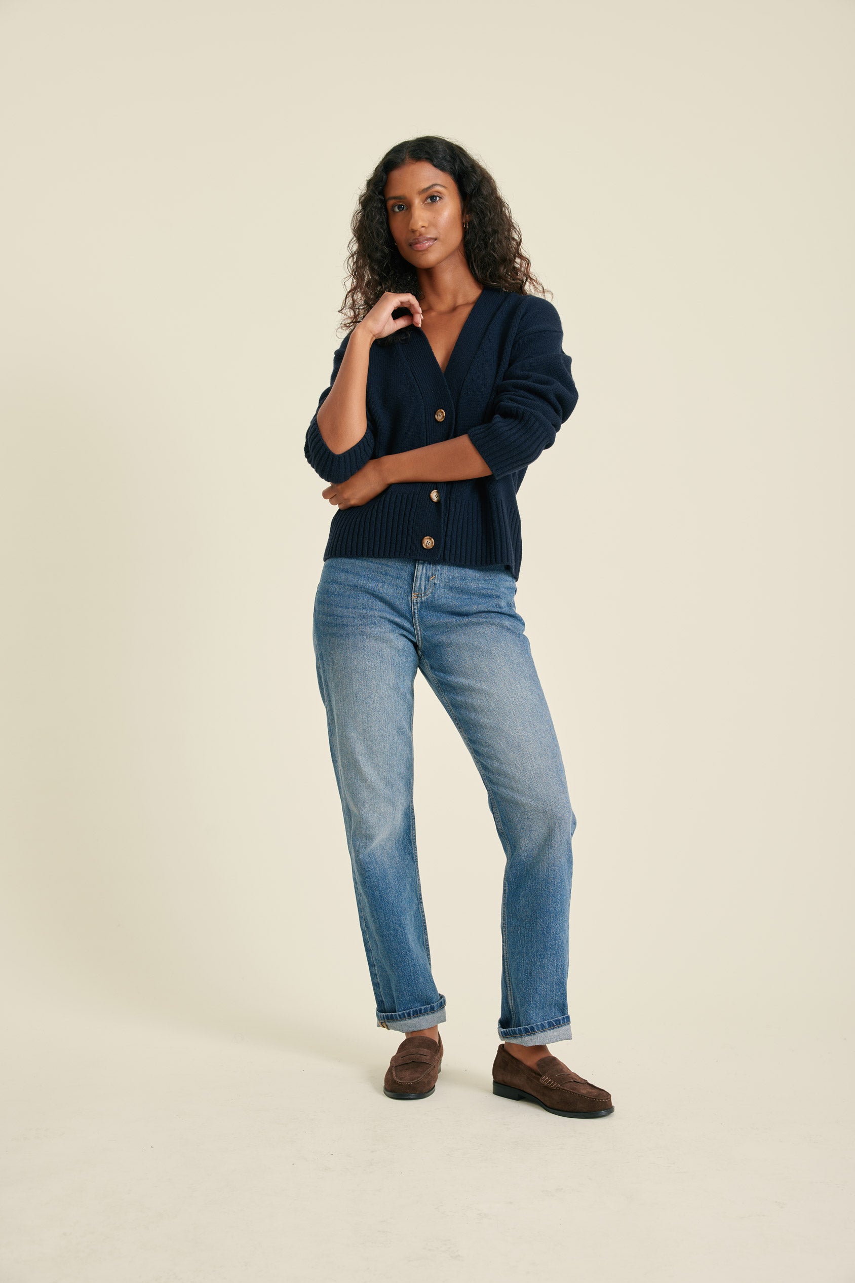 Woman wearing a navy blazer and blue jeans on a beige background