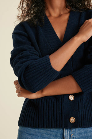 Person wearing a navy blue cardigan with gold buttons on a beige background