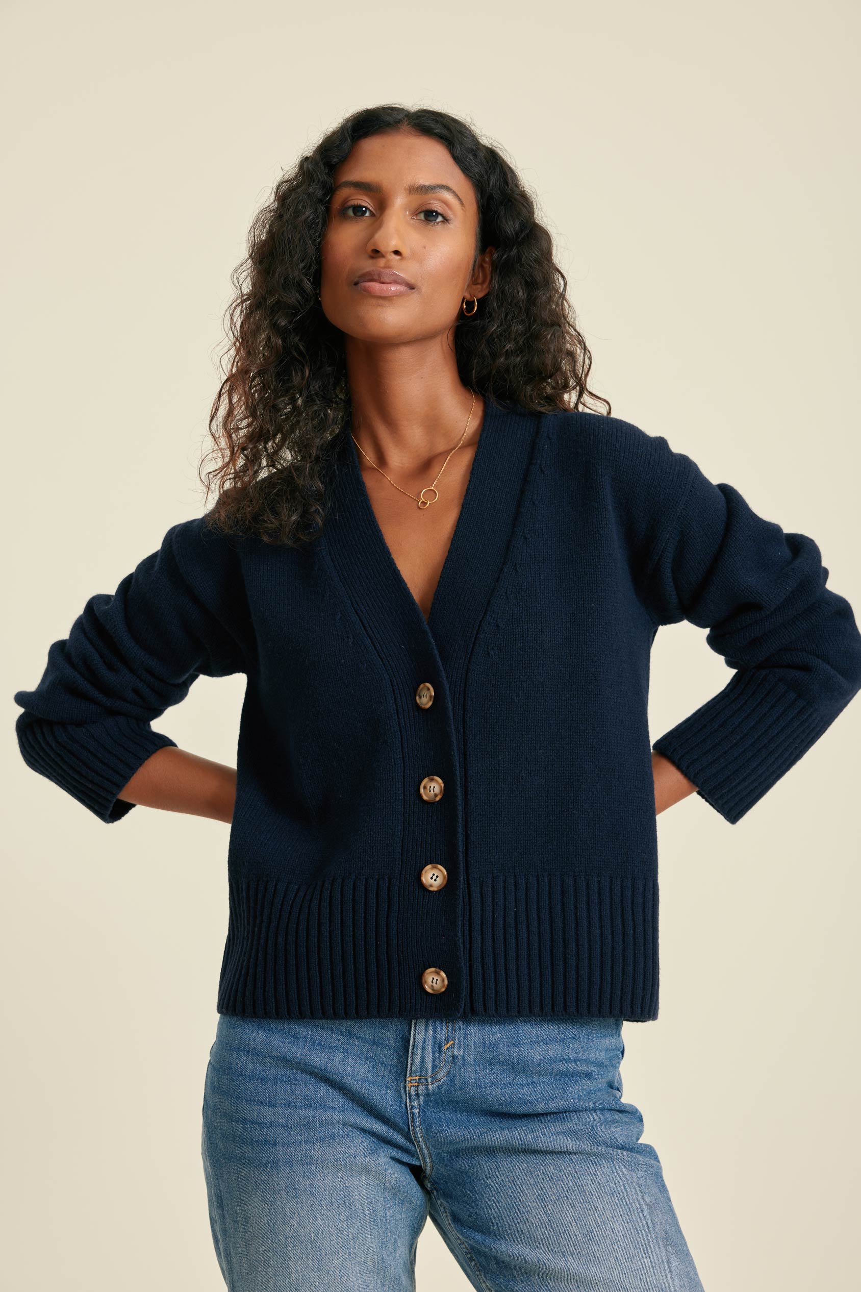 Woman wearing a navy cardigan with gold buttons on a beige background