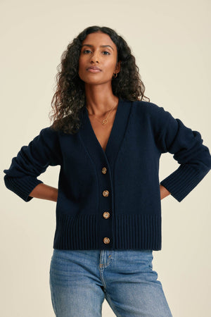 Woman wearing a navy cardigan with gold buttons on a beige background