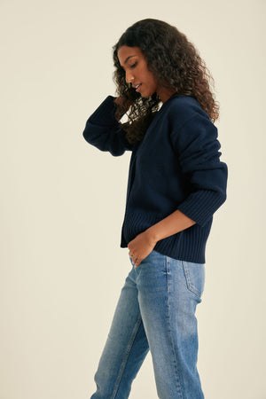 Woman wearing a navy sweater and blue jeans on a beige background