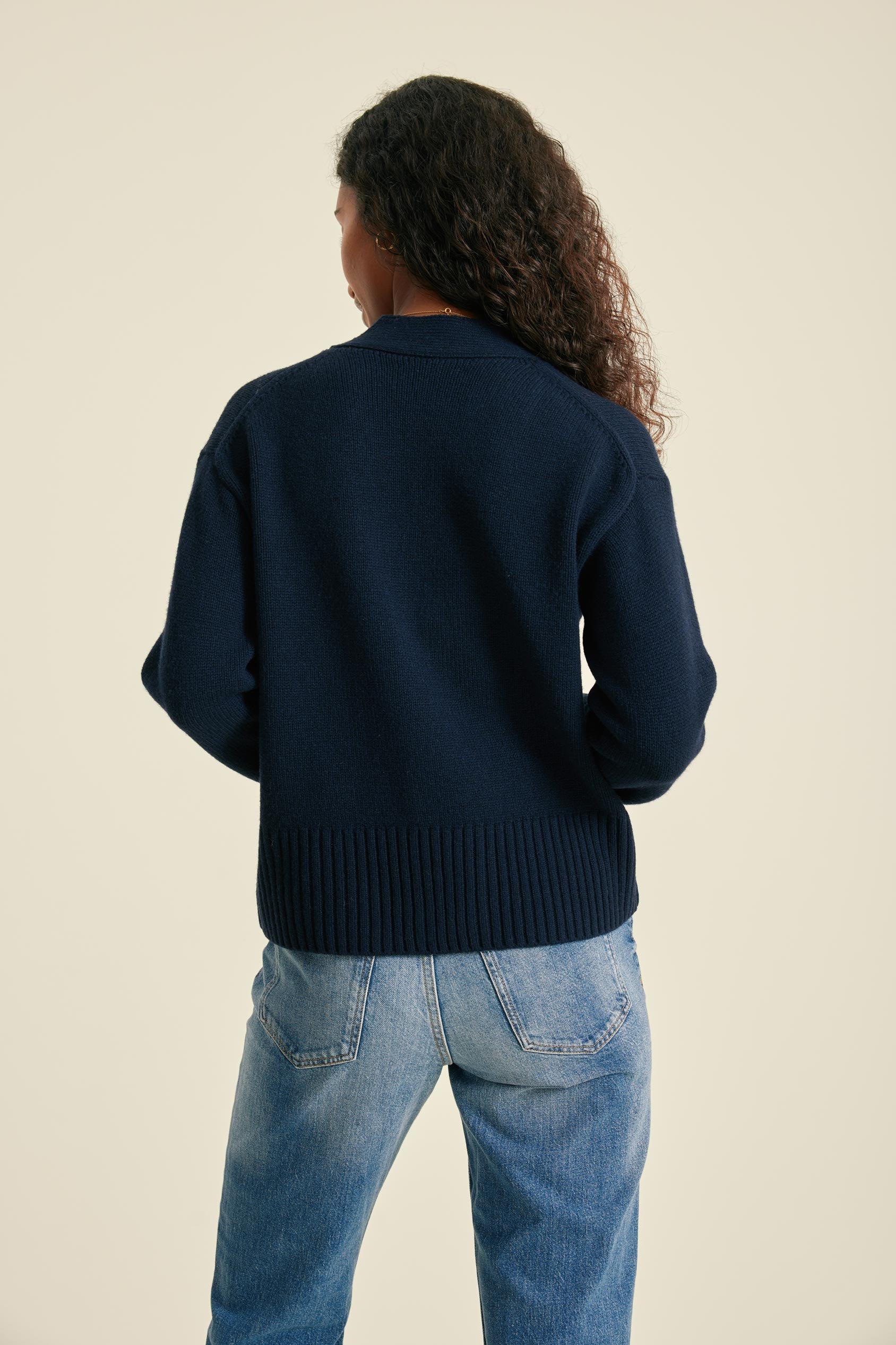 Person wearing a navy sweater and blue jeans on a beige background