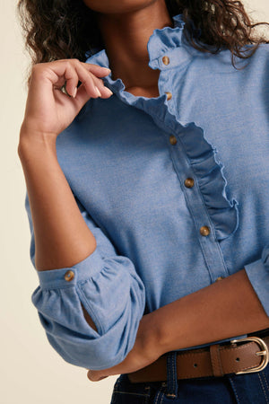 Close-up of a person wearing a blue denim shirt with ruffled details.