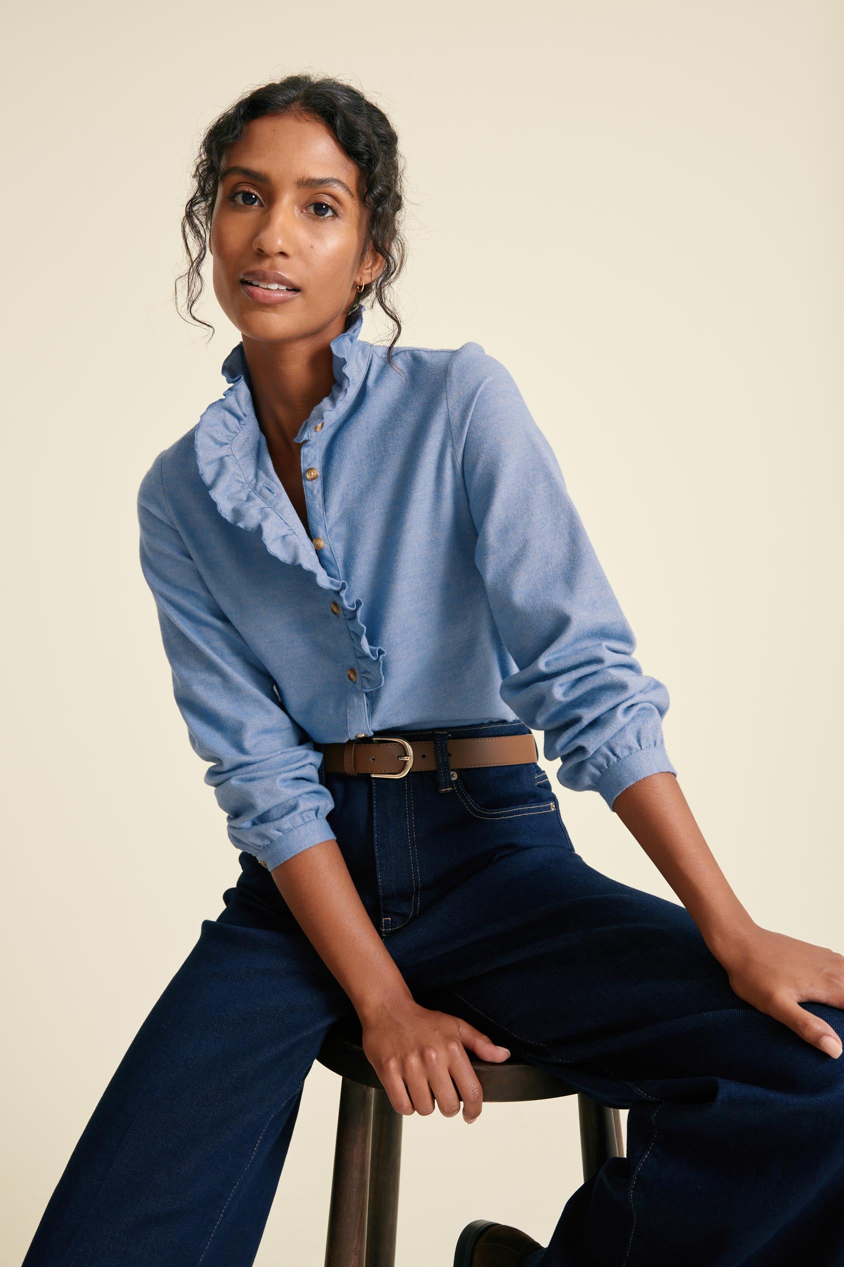 Woman wearing a blue shirt and dark jeans on a beige background