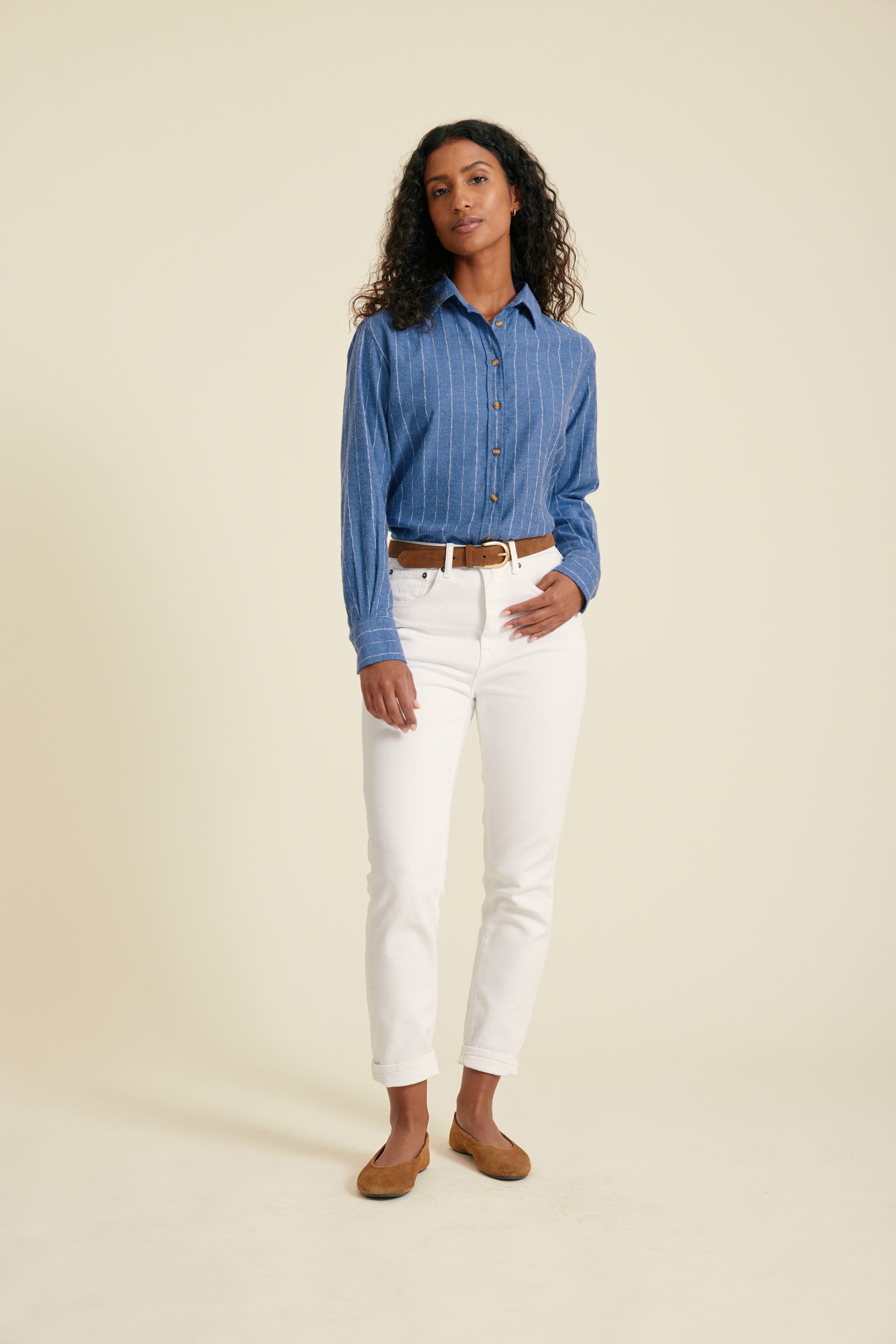 Woman wearing a blue striped shirt and white pants on a beige background