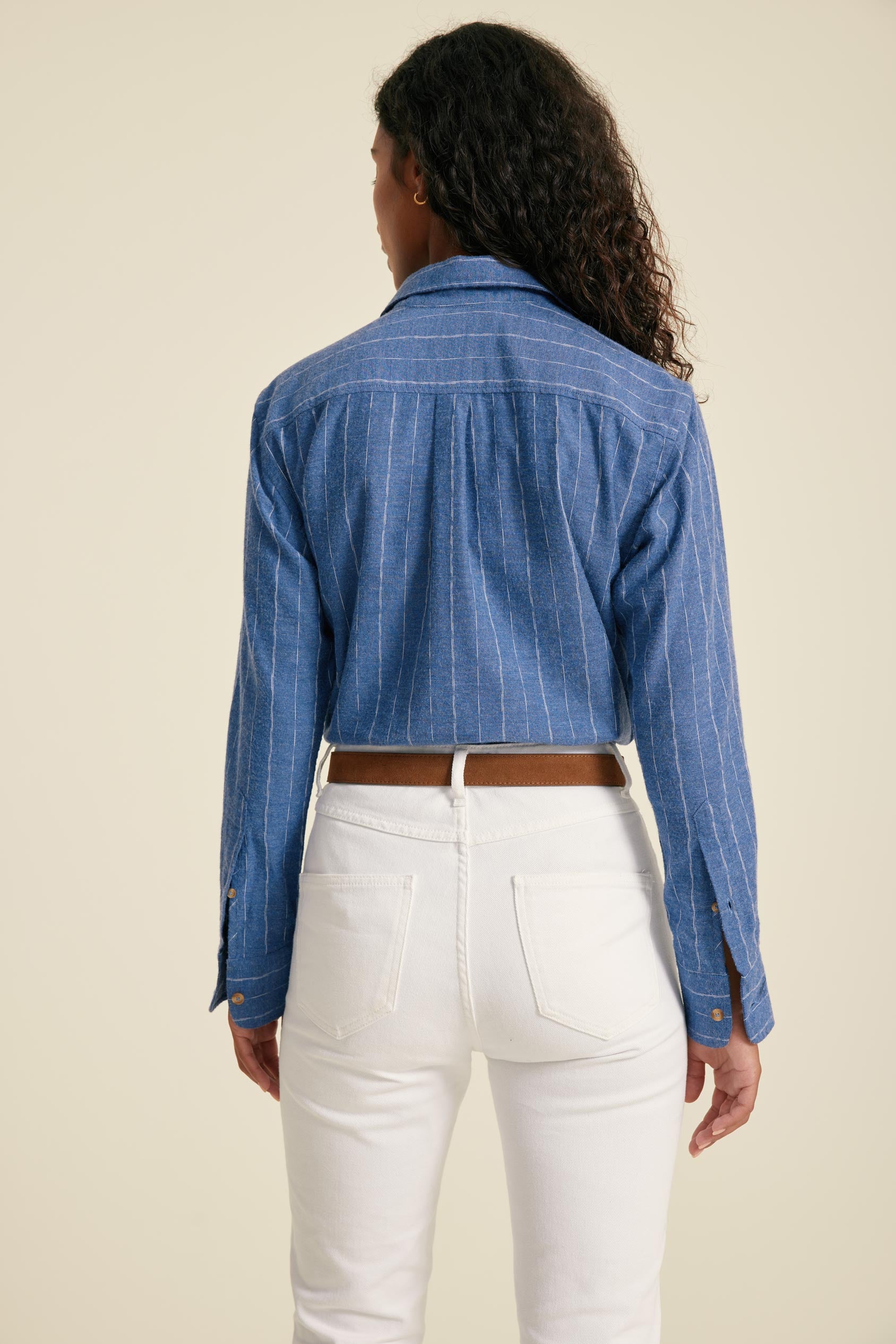 Person wearing a blue striped shirt and white pants on a beige background