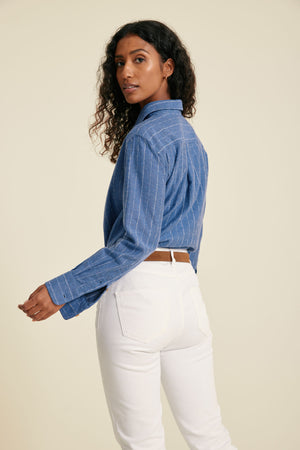 Woman wearing a blue striped shirt and white pants on a beige background