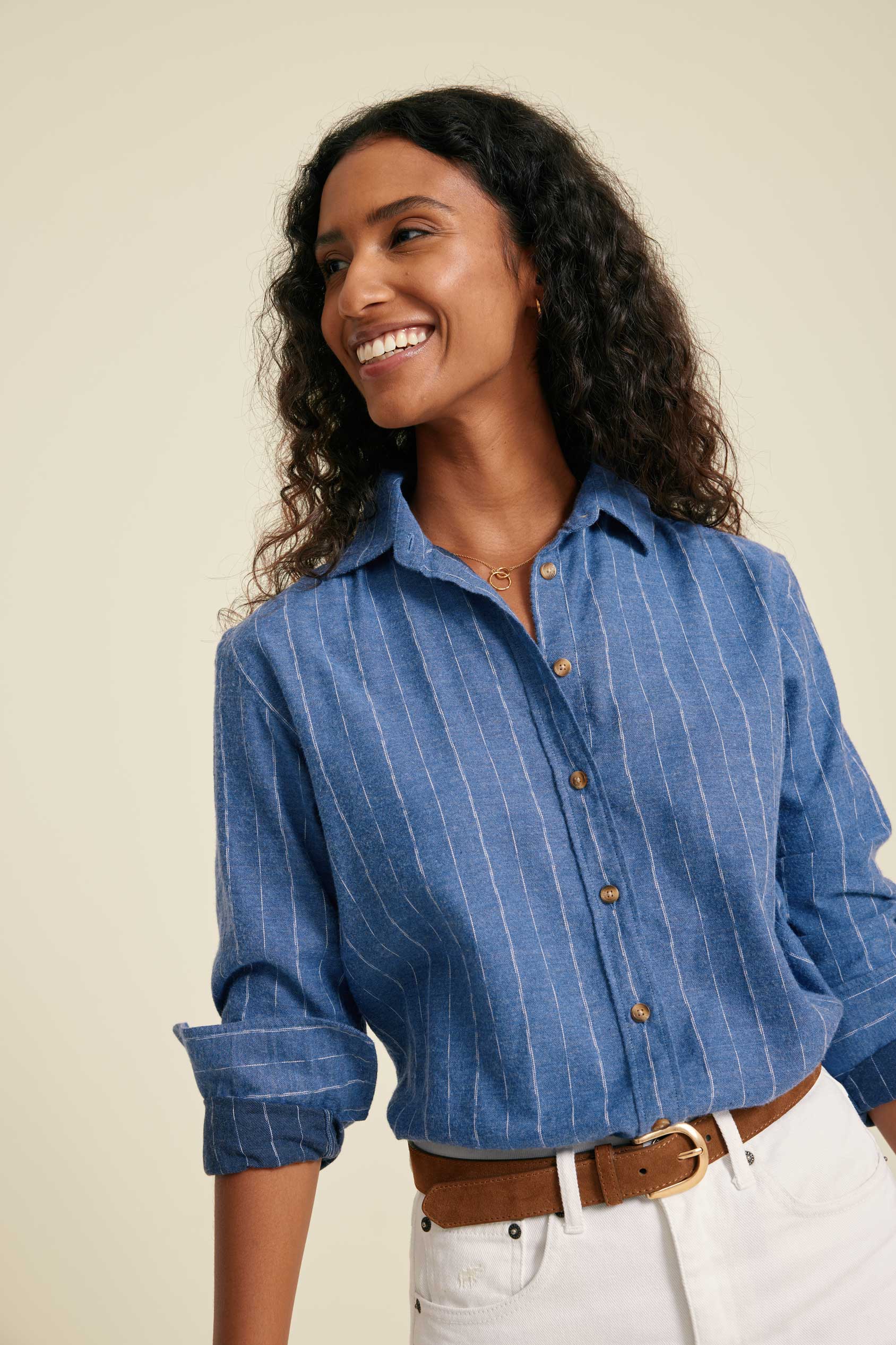 Woman wearing a blue striped shirt with rolled-up sleeves against a beige background
