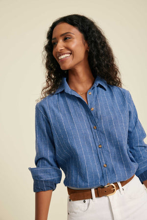 Woman wearing a blue striped shirt with rolled-up sleeves against a beige background