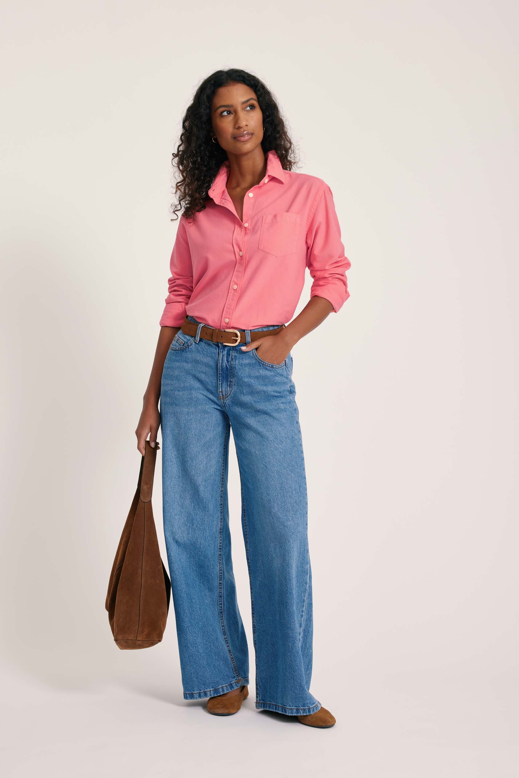 Woman wearing a pink shirt and blue jeans holding a brown bag on a white background