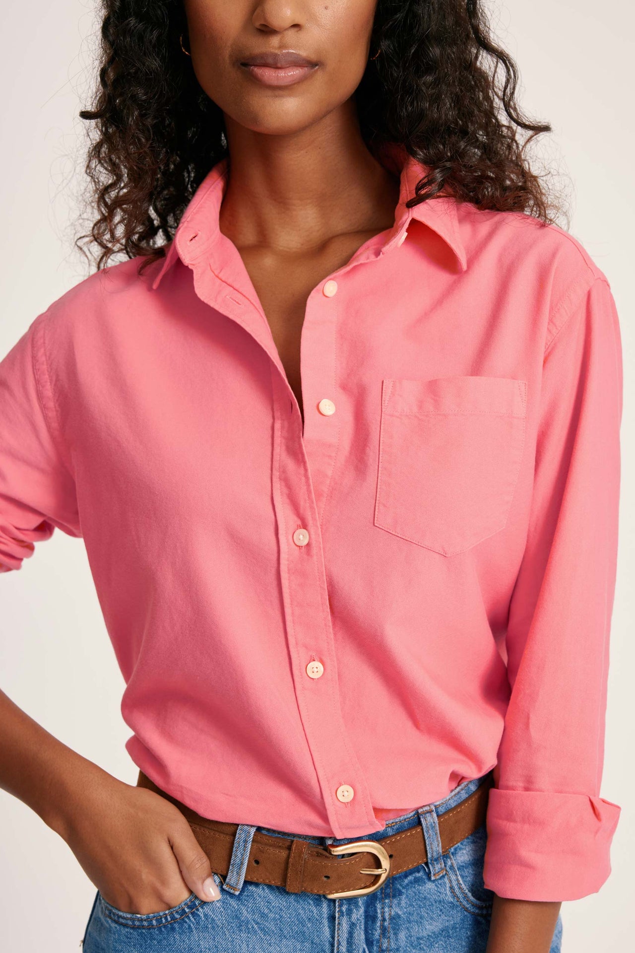 Woman wearing a pink button-up shirt and blue jeans against a plain background