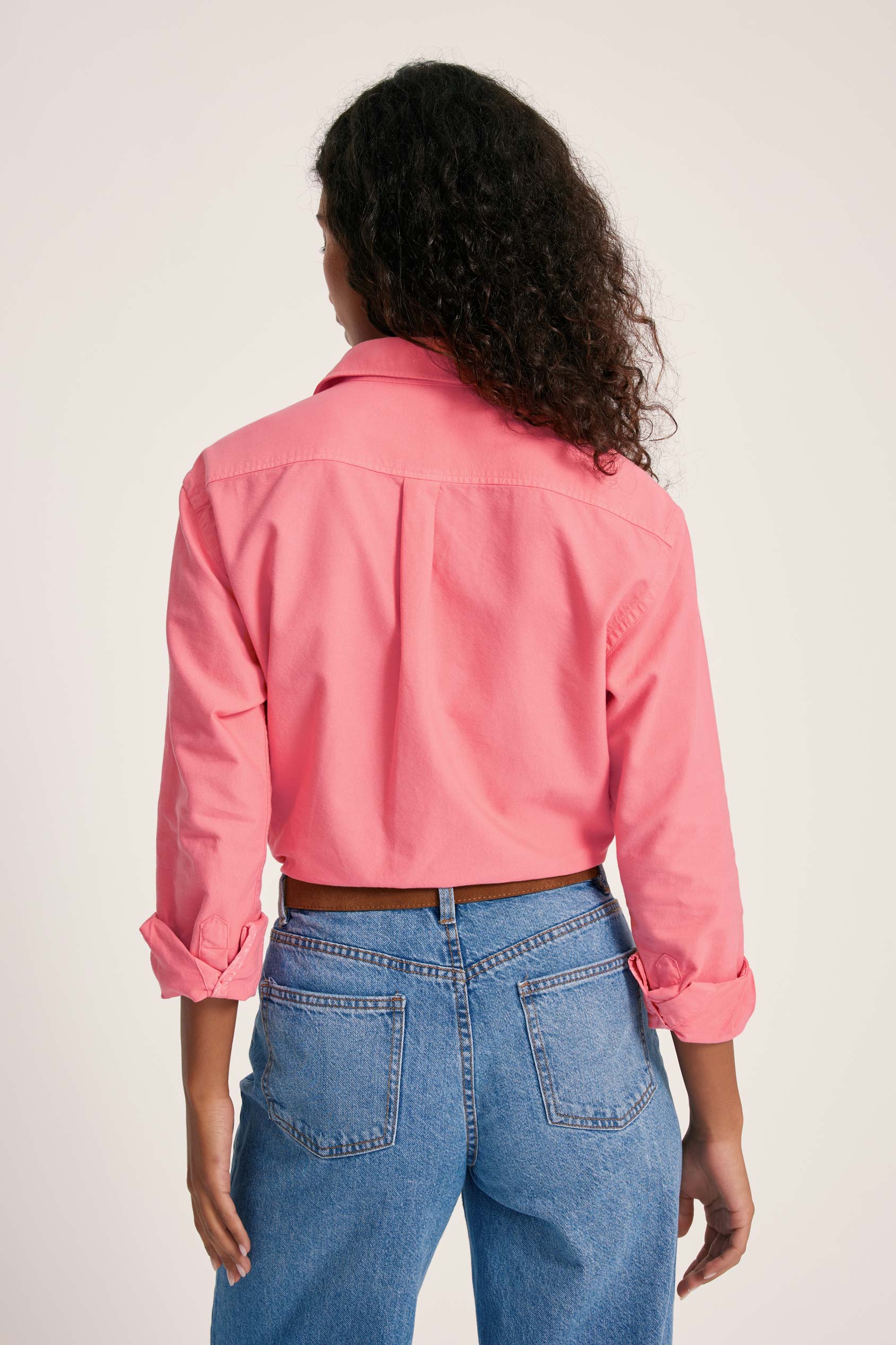 Person wearing a pink jacket and blue jeans on a plain background