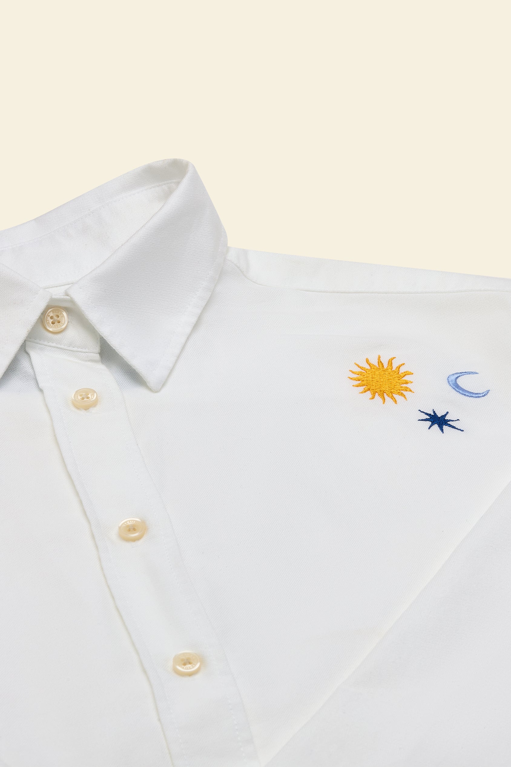 White shirt with embroidered sun, moon, and star designs on a beige background