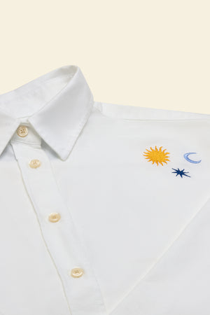 White shirt with embroidered sun, moon, and star designs on a beige background