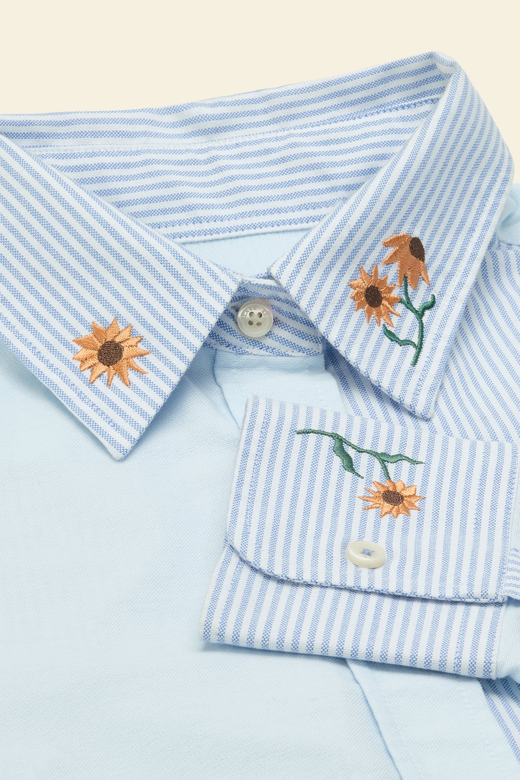 Light blue striped shirt with floral embroidery on a beige background