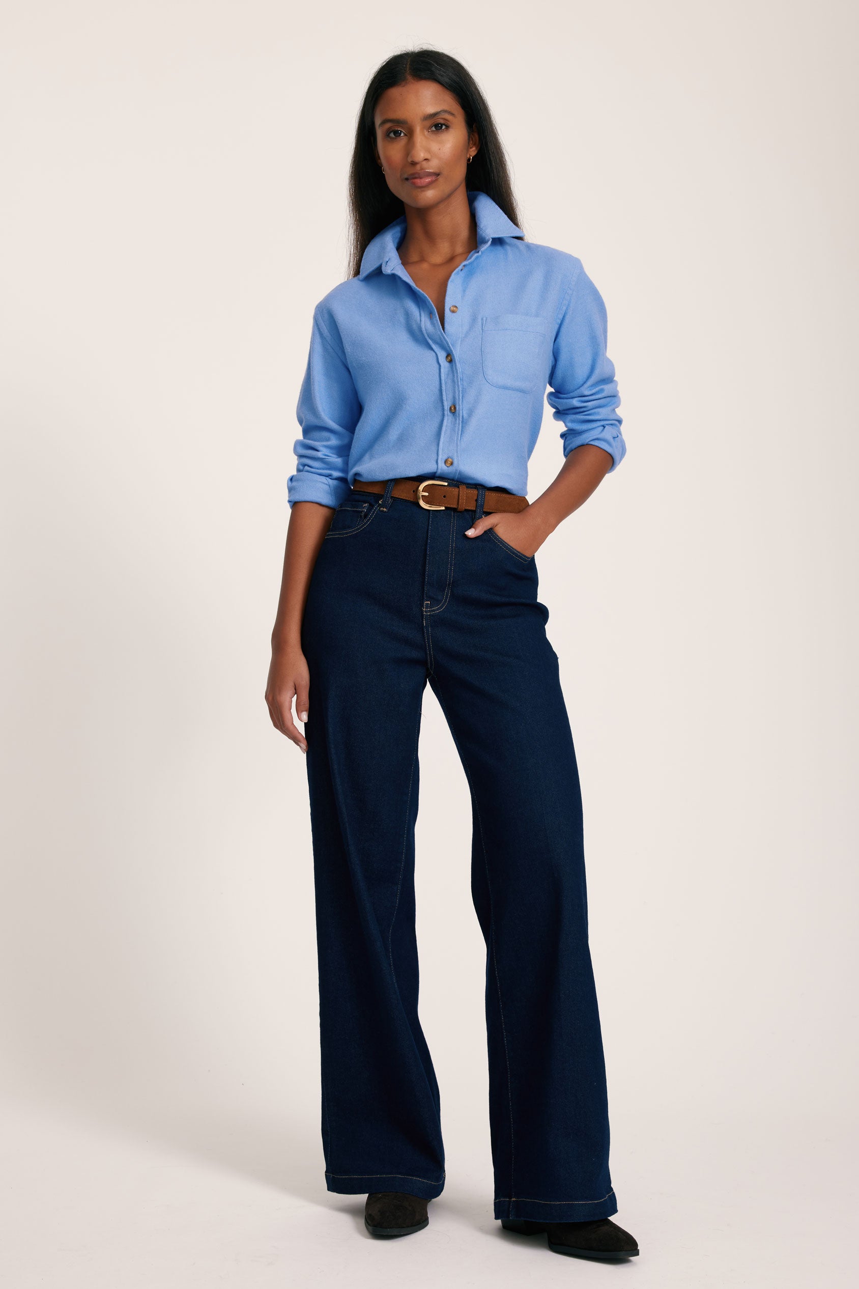 Woman wearing a blue shirt and dark jeans on a white background