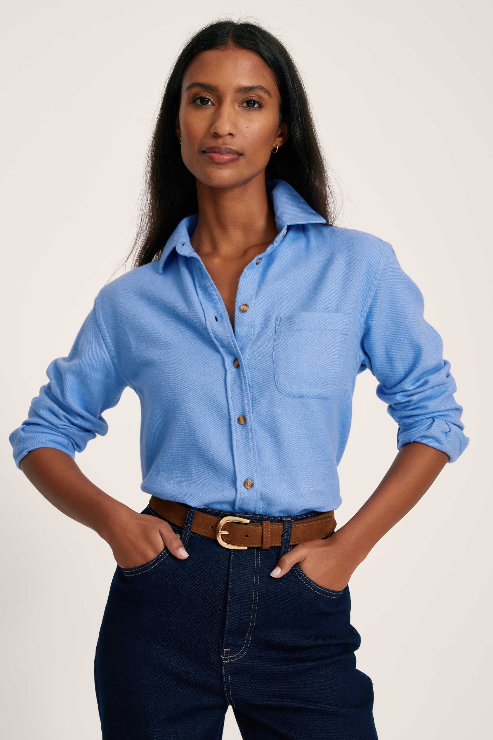 Woman wearing a light blue button-up shirt and dark jeans on a plain background