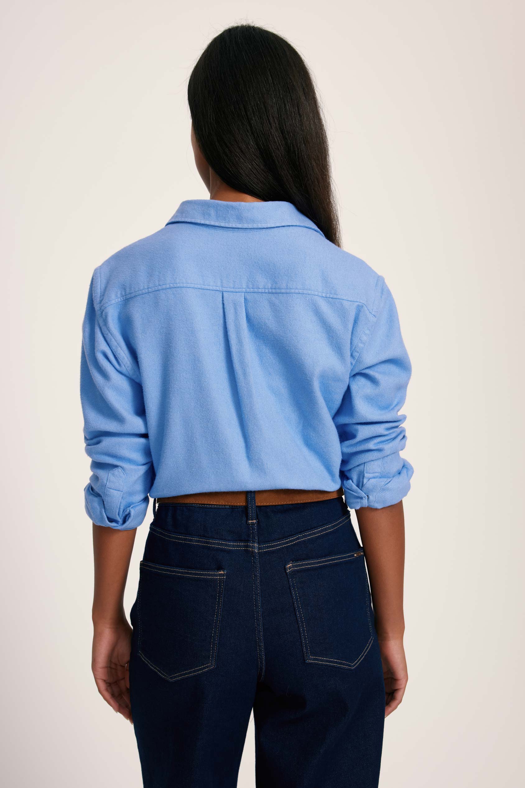 Person wearing a light blue denim jacket and dark jeans on a plain background