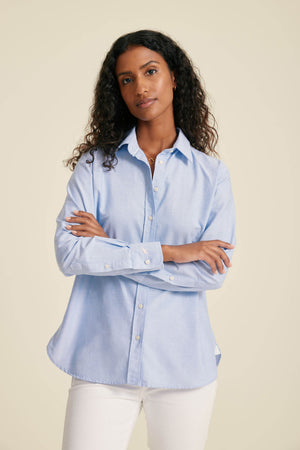 Woman wearing a light blue button-up shirt against a beige background