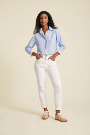 Woman wearing a light blue shirt and white pants against a beige background