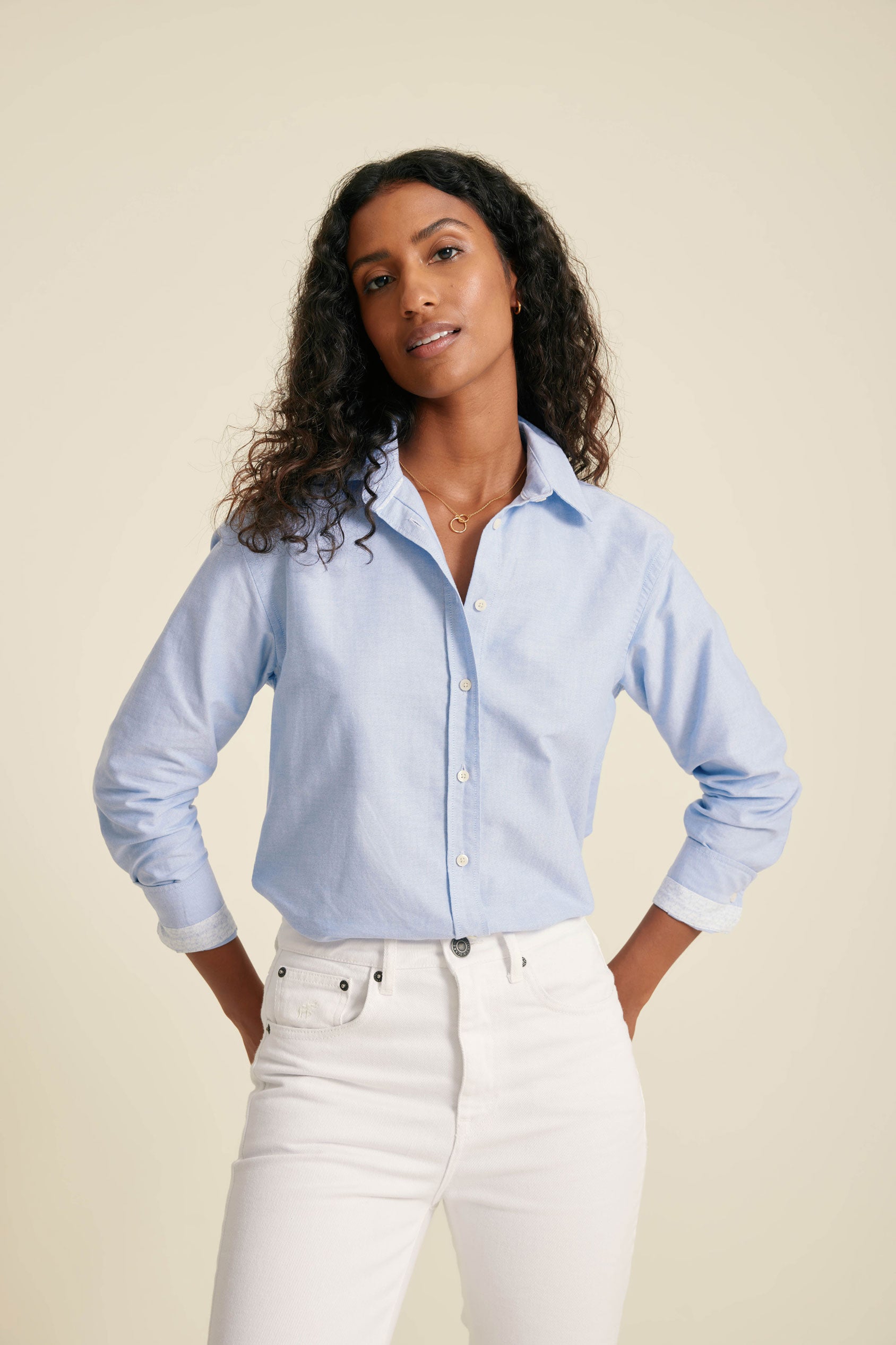Woman wearing a light blue button-up shirt and white pants against a beige background