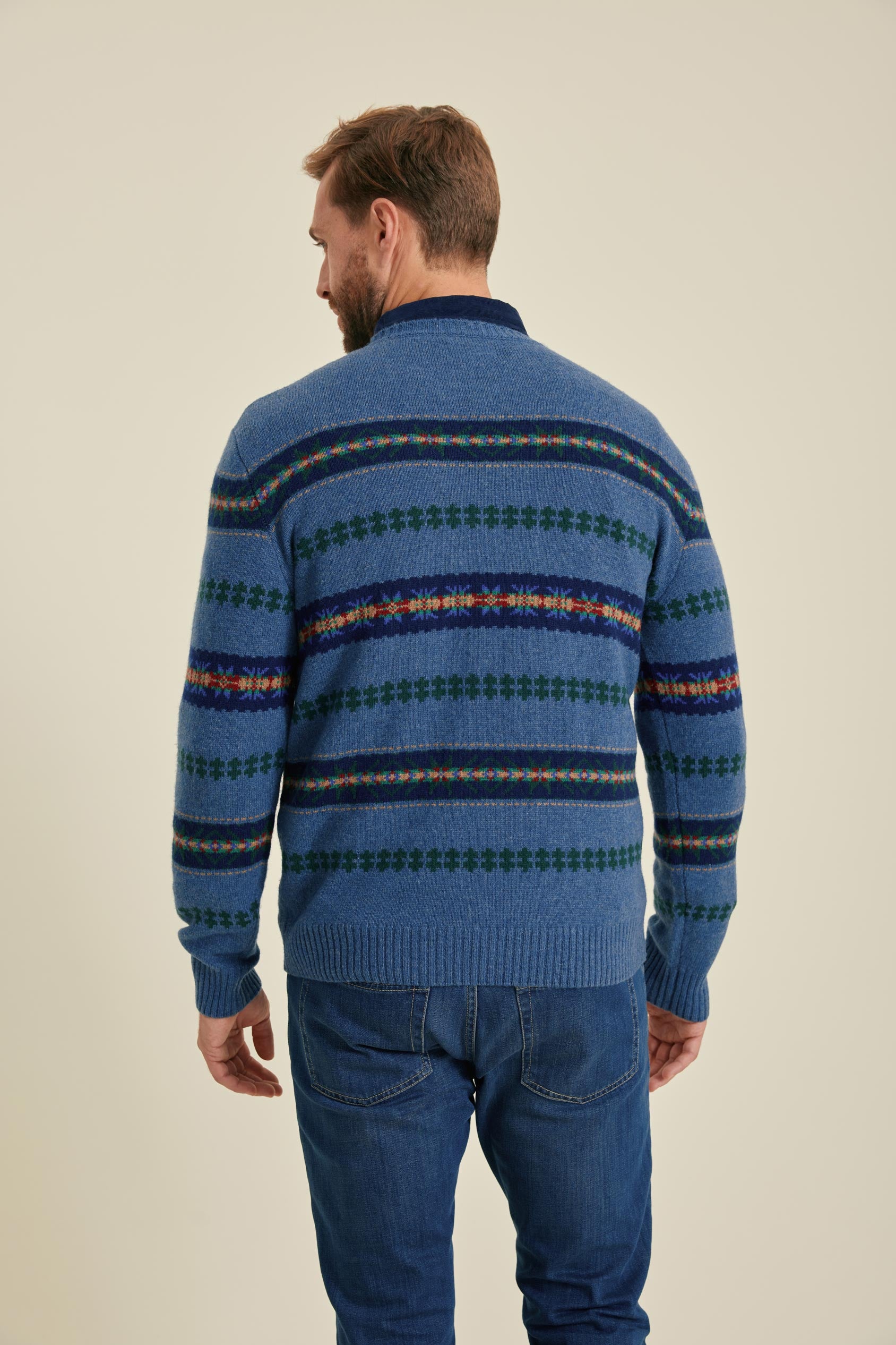 Man wearing a blue patterned sweater and jeans on a beige background