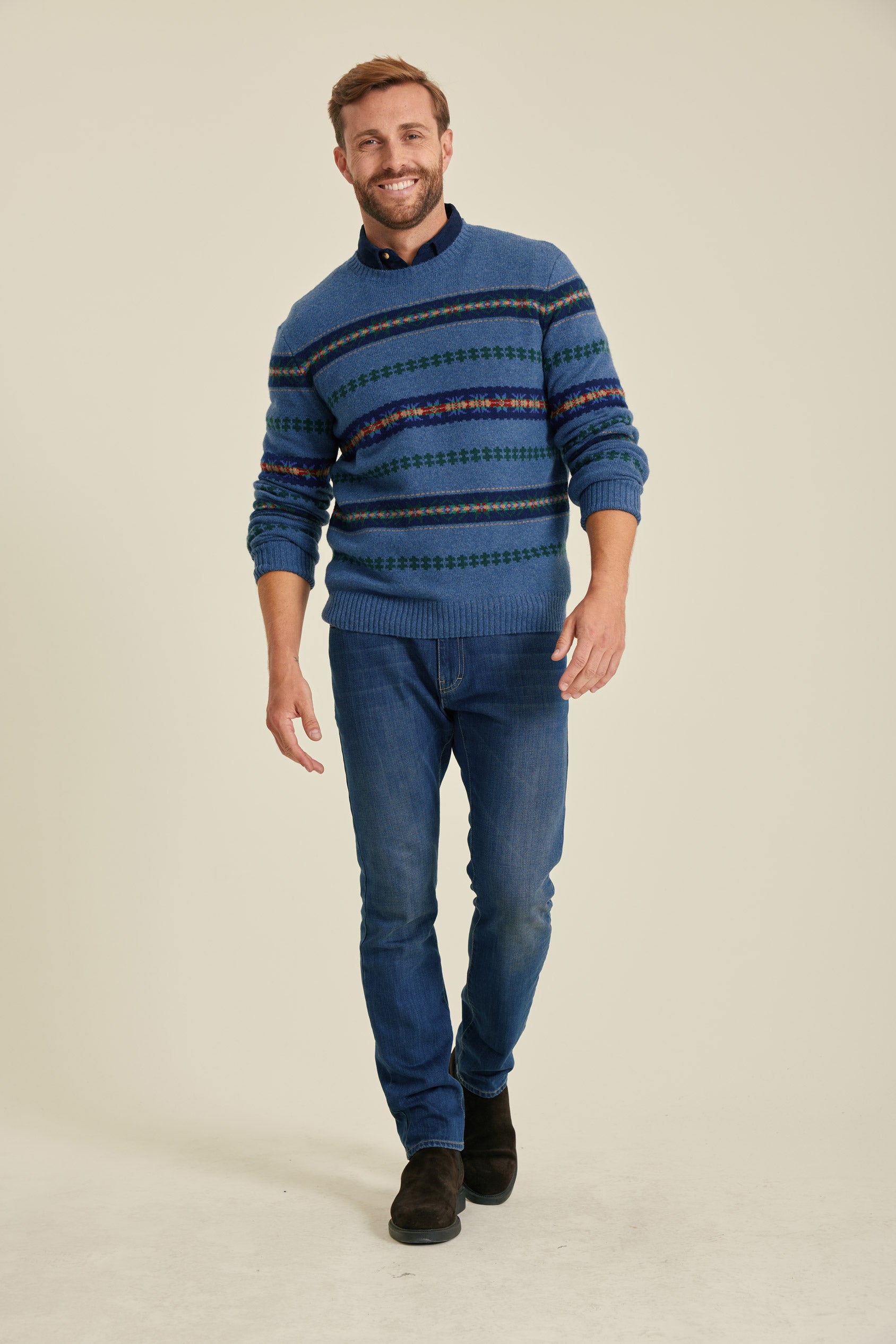 Man wearing a blue patterned sweater and jeans on a beige background