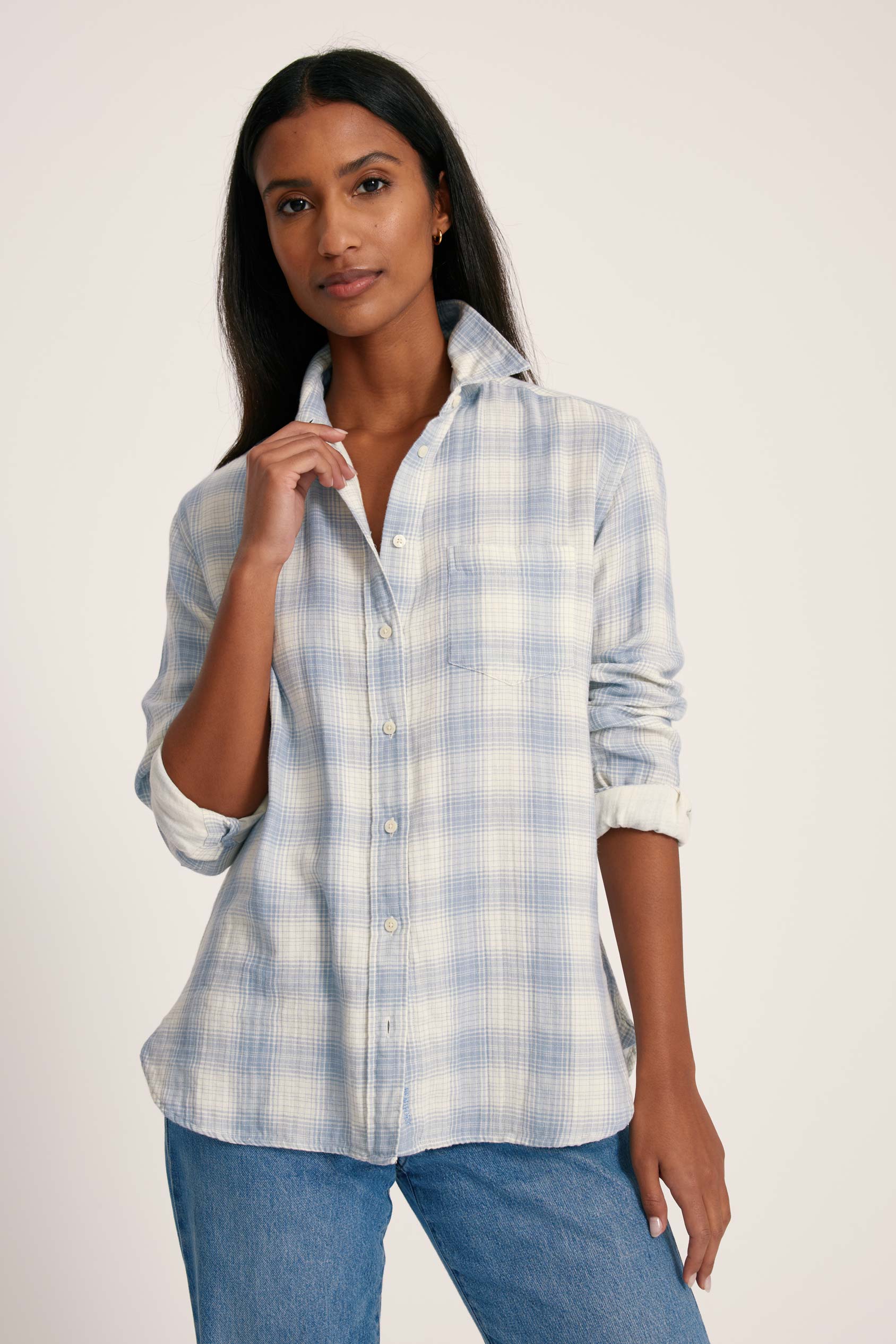 Woman wearing a blue and white checkered shirt with rolled-up sleeves on a plain background
