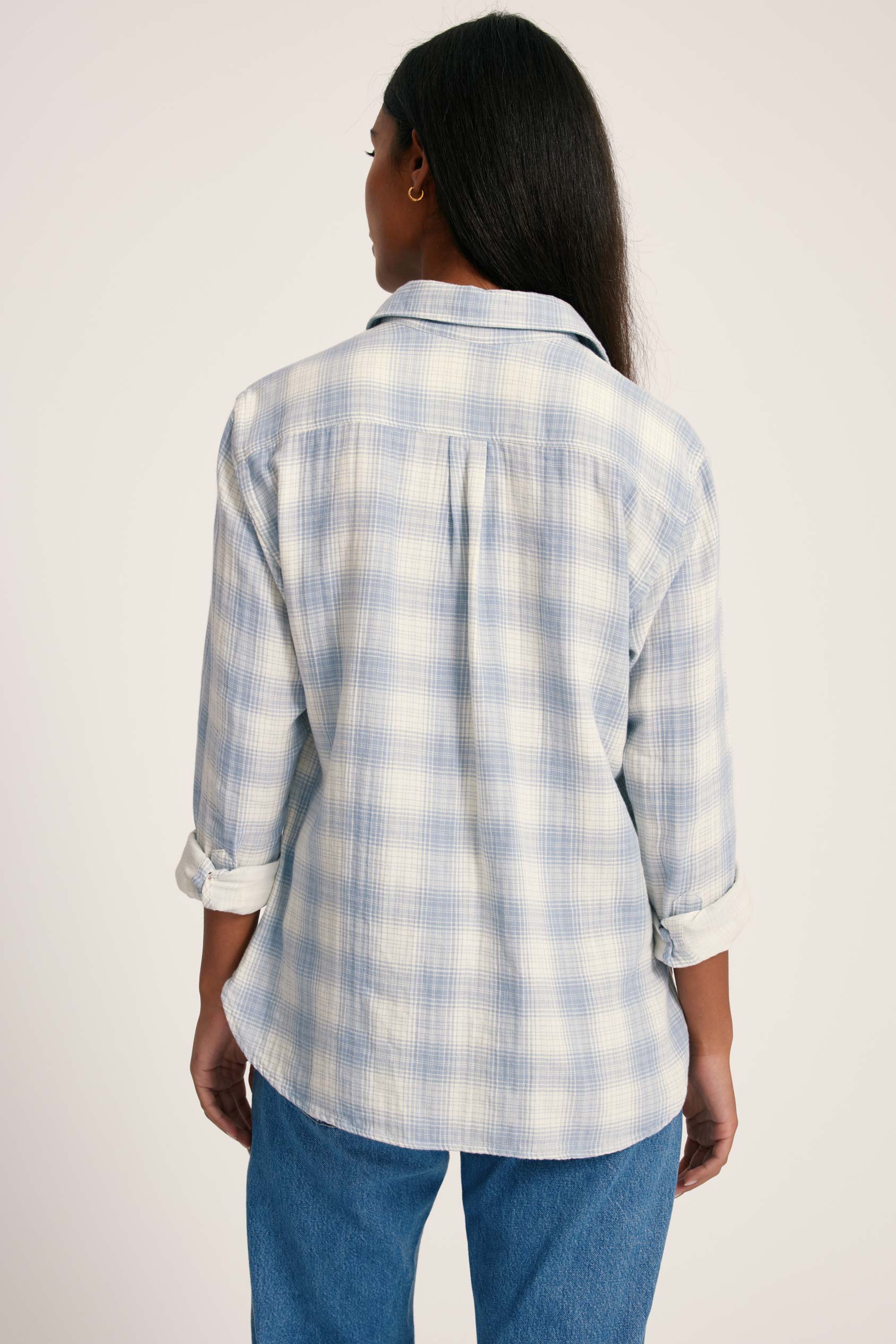 Person wearing a blue and white plaid shirt with rolled-up sleeves on a plain background
