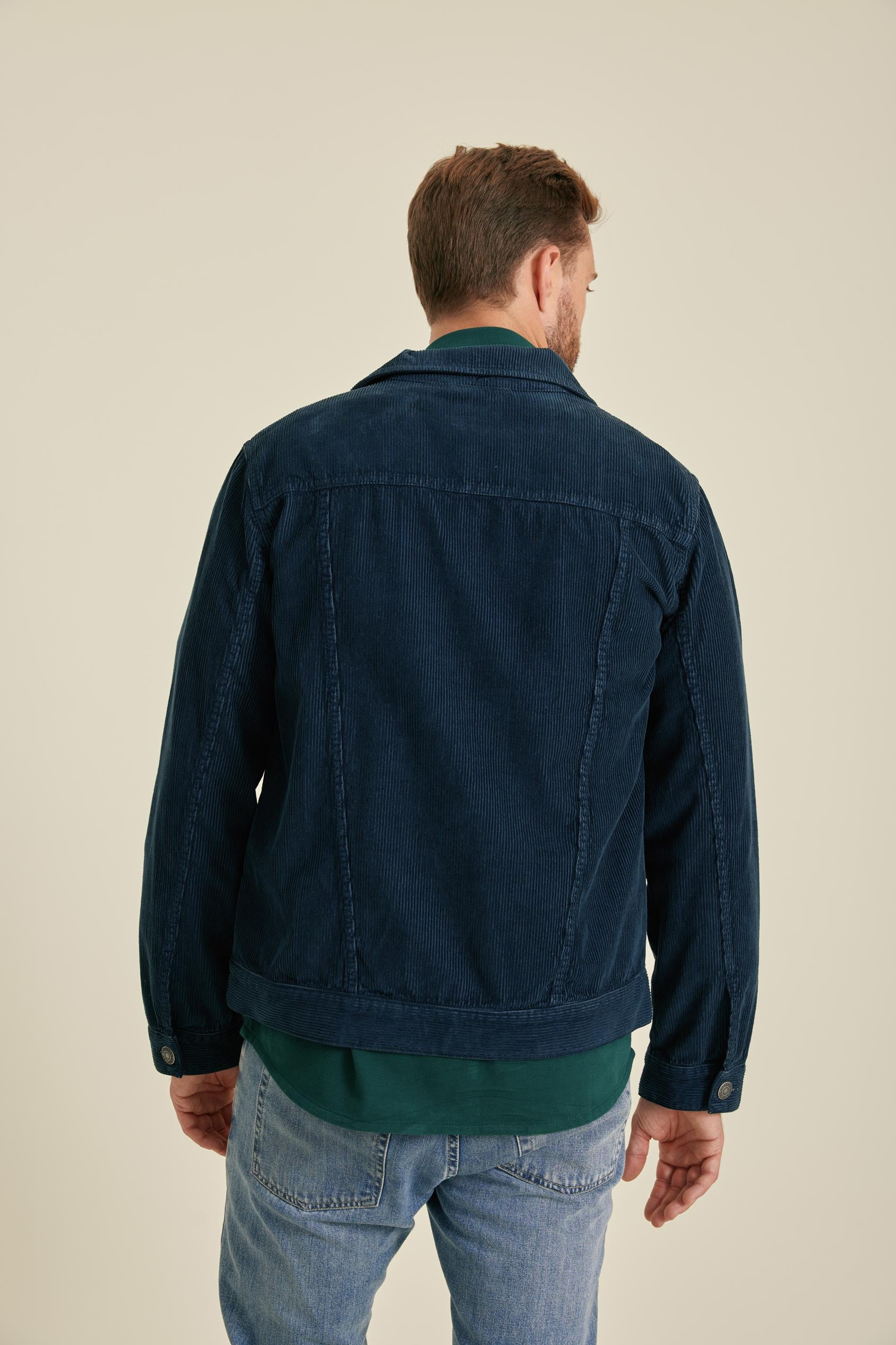 Man wearing a dark blue jacket and light blue jeans on a beige background