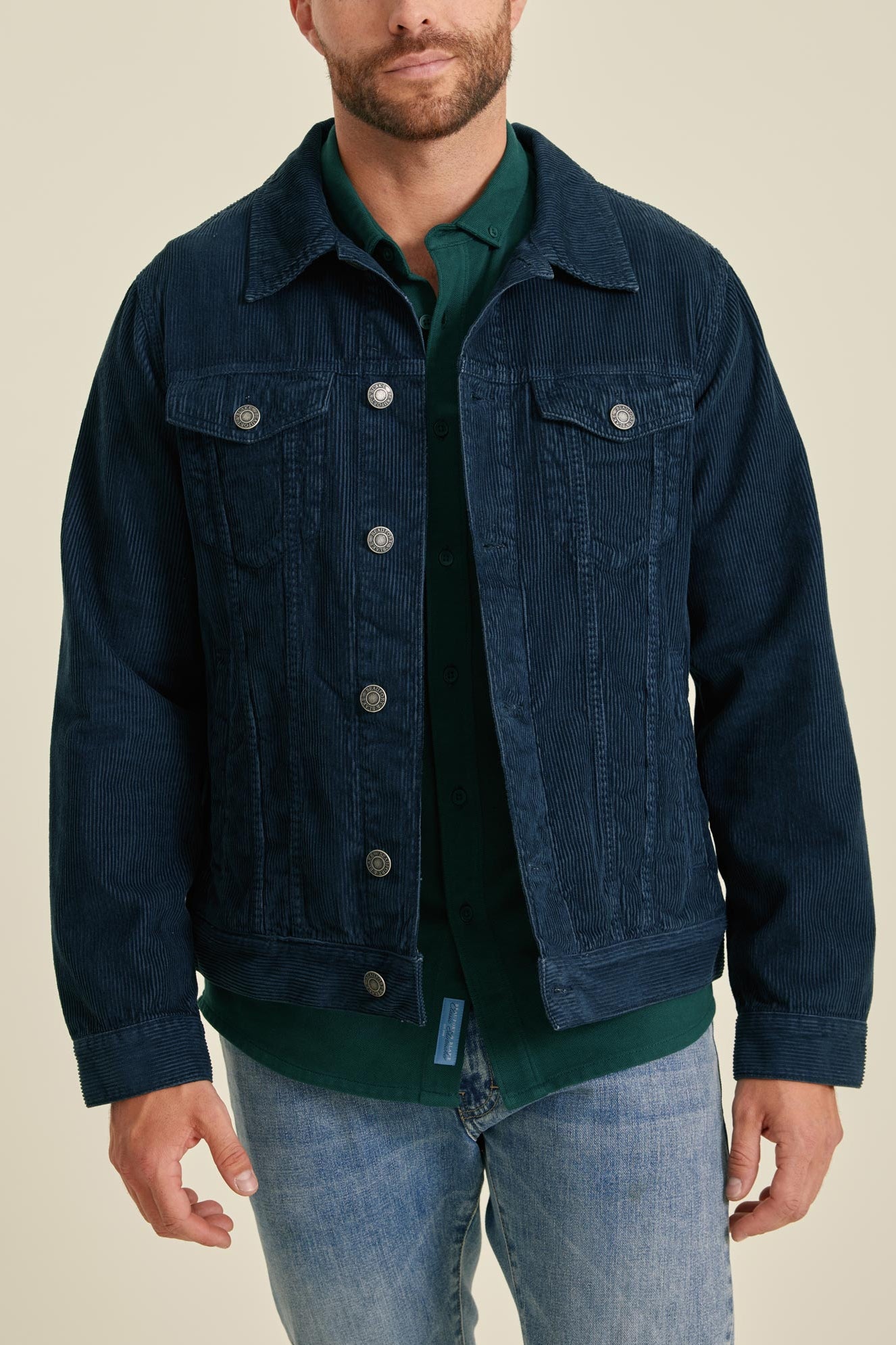Man wearing a dark blue denim jacket over a green shirt on a beige background