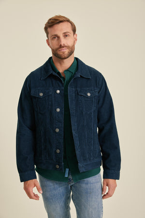 Man wearing a dark blue denim jacket over a green shirt on a beige background