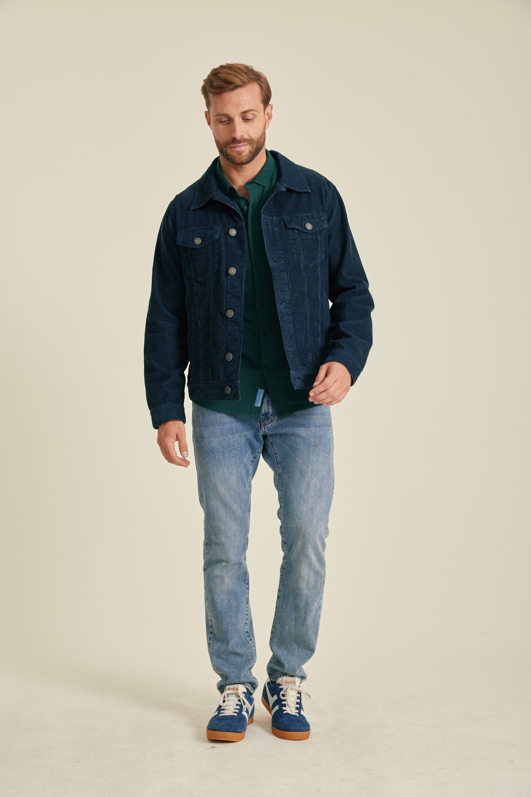 Man wearing a denim jacket, green shirt, and blue jeans on a beige background
